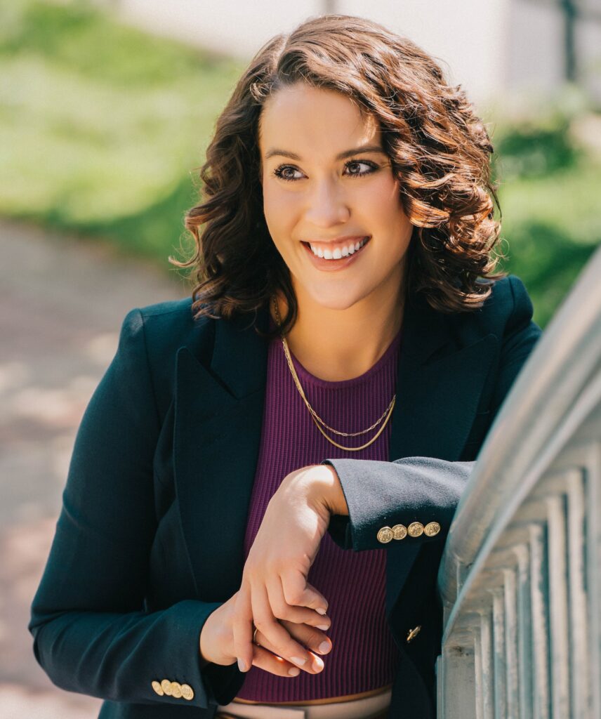 Katie Maslechko, smiling and leaning against a railing. 