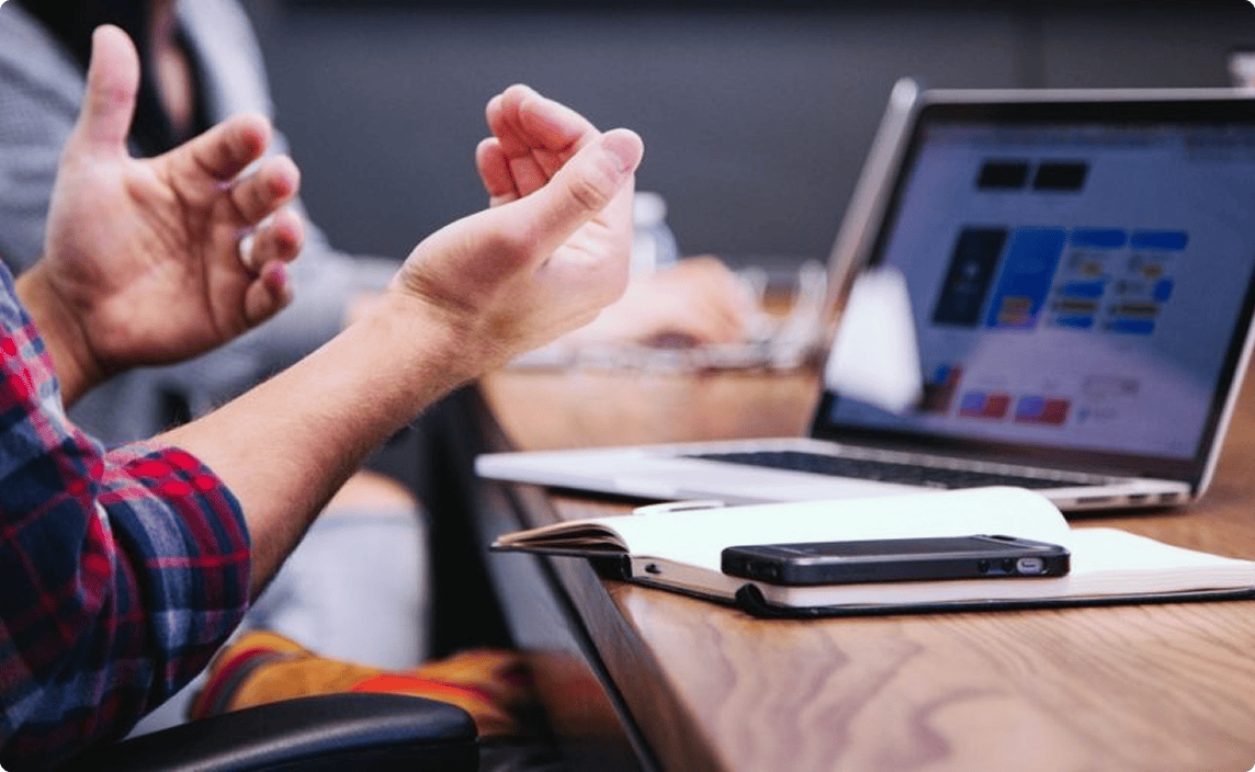 A person using their hands to talk in front of a laptop screen