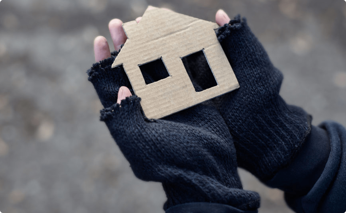 A person holding a small house made out of cardboard.