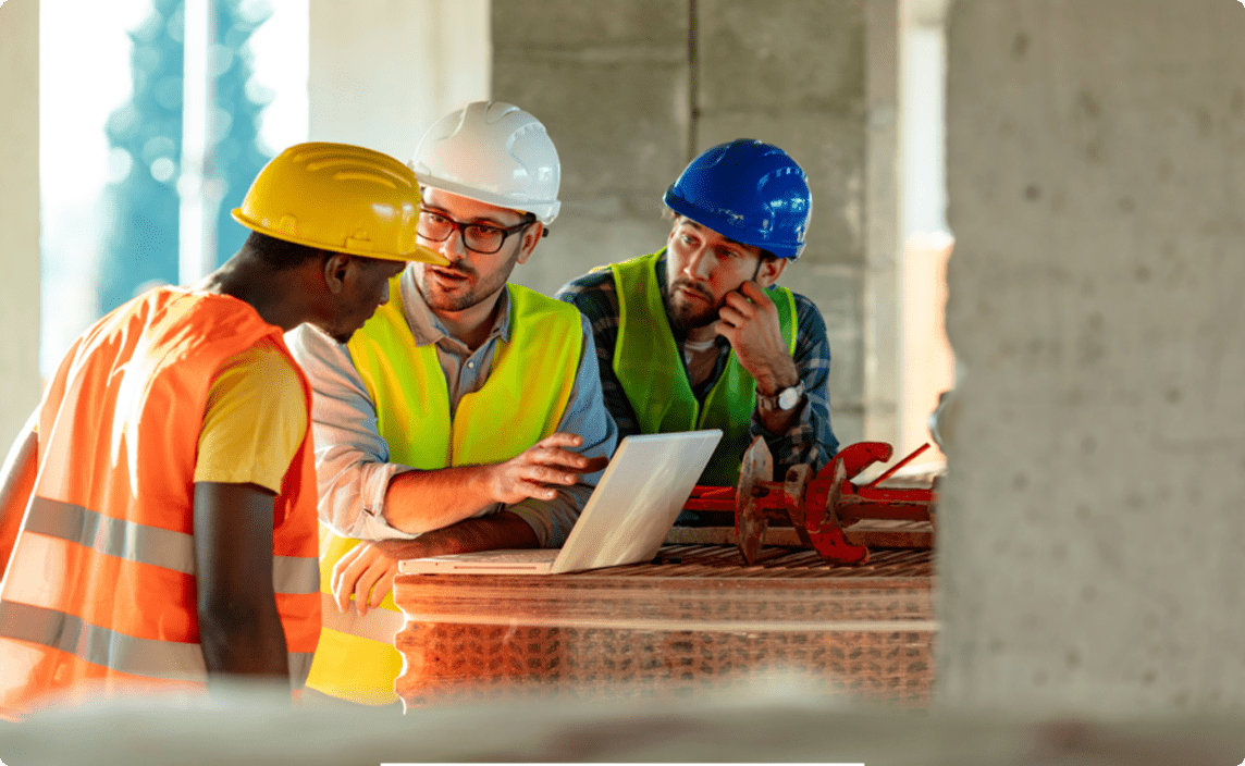 A group of workers discussing a plan over a laptop at a job site.