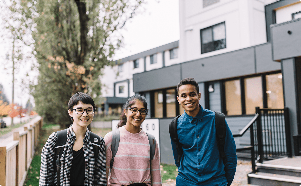 Three youths smiling in front of a residence.
