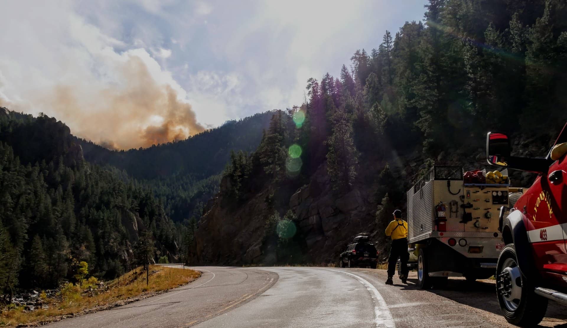 A road with smoke from a wildfire in the distance.